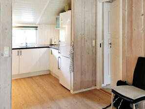 A kitchen with wooden cabinets, a refrigerator, a sink, and a chair.