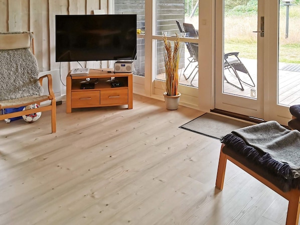 A living room with a television, wooden furniture, a potted plant, and a view through a glass door.