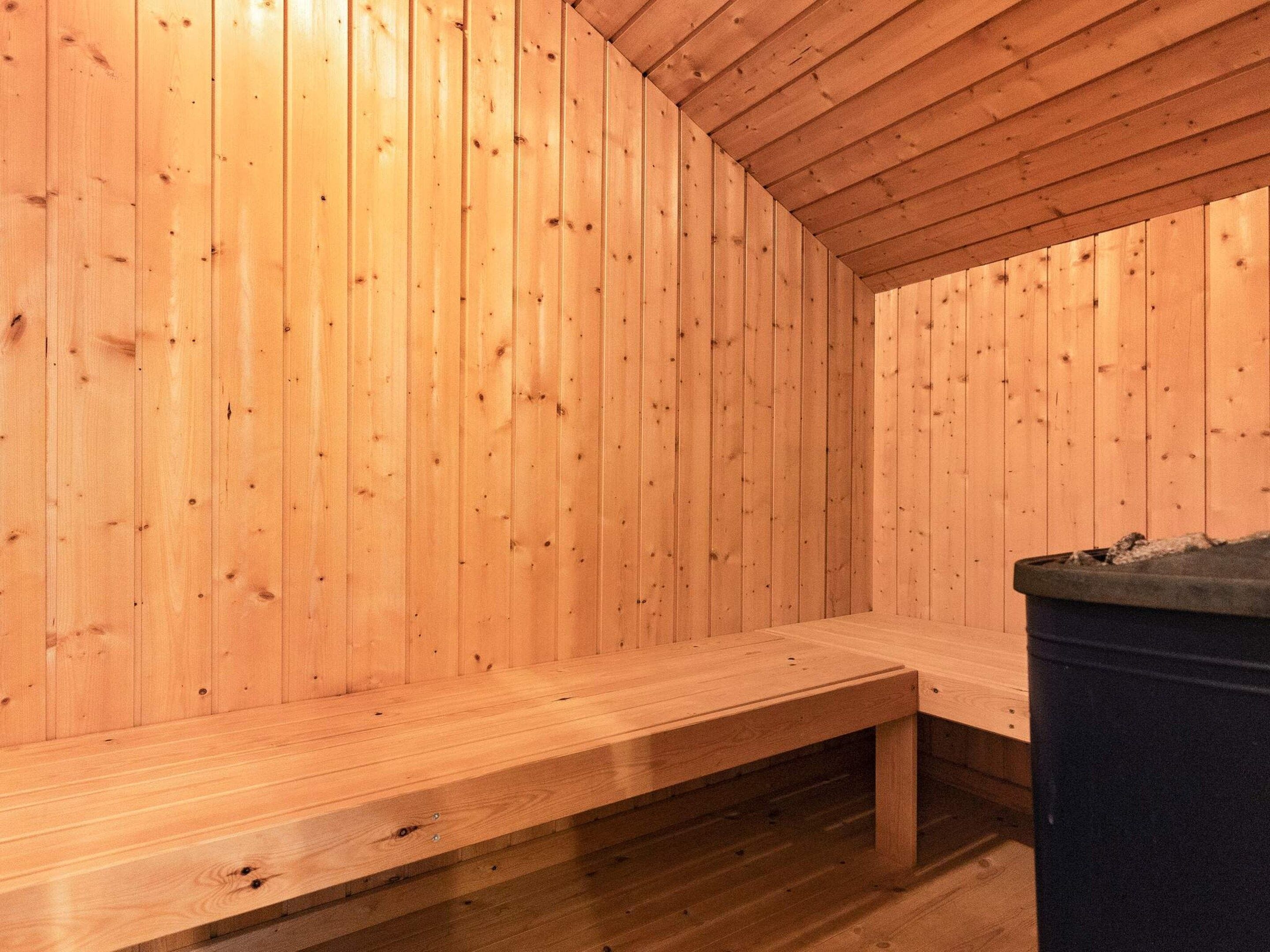 A wooden sauna room with a bench and a trash bin.