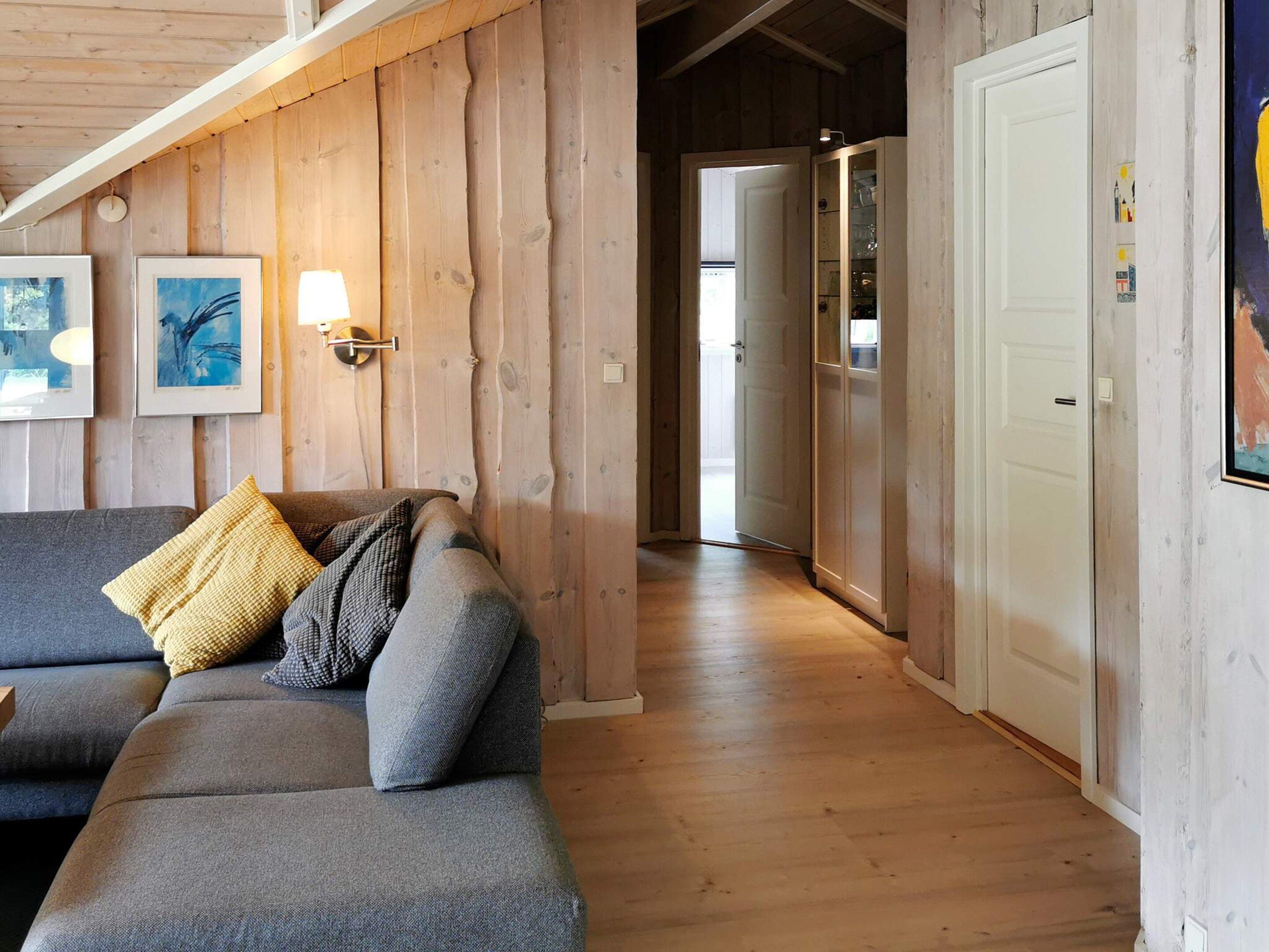 A wooden interior with a sofa, a wall-mounted light, and a door leading to another room.