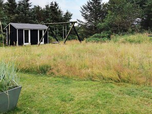 A rustic wooden structure with a sloped roof, surrounded by tall grass and dense trees.