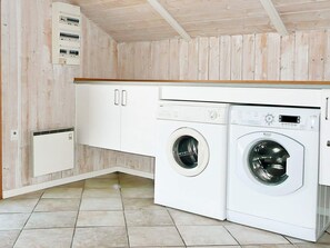 A laundry room with two white washing machines, a white cabinet, and a white electrical panel on the wall.