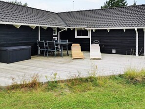 A covered outdoor area with a table and chairs, a wooden bench, and a small basketball hoop.