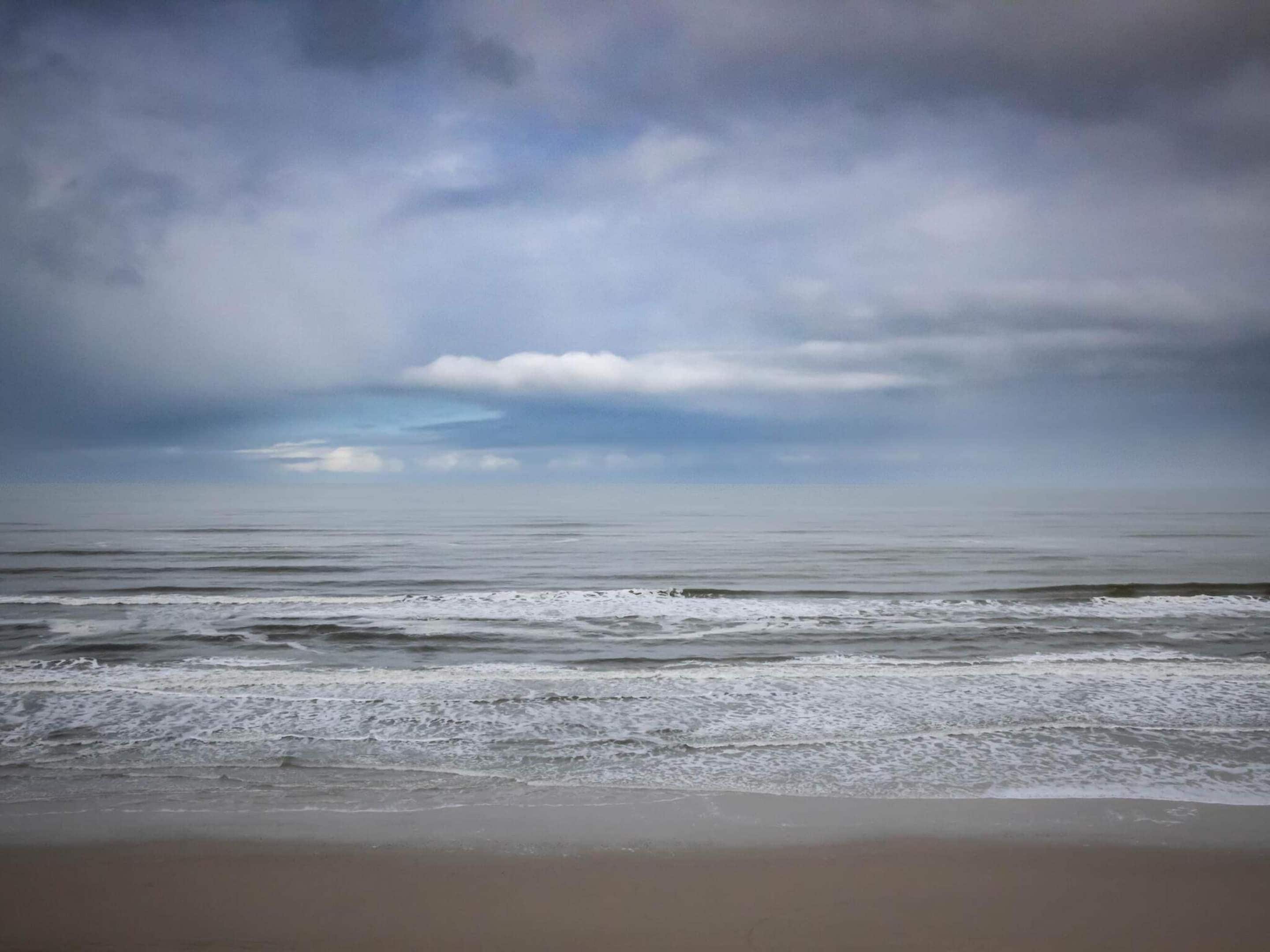 A beach with waves approaching the shore under a cloudy sky.