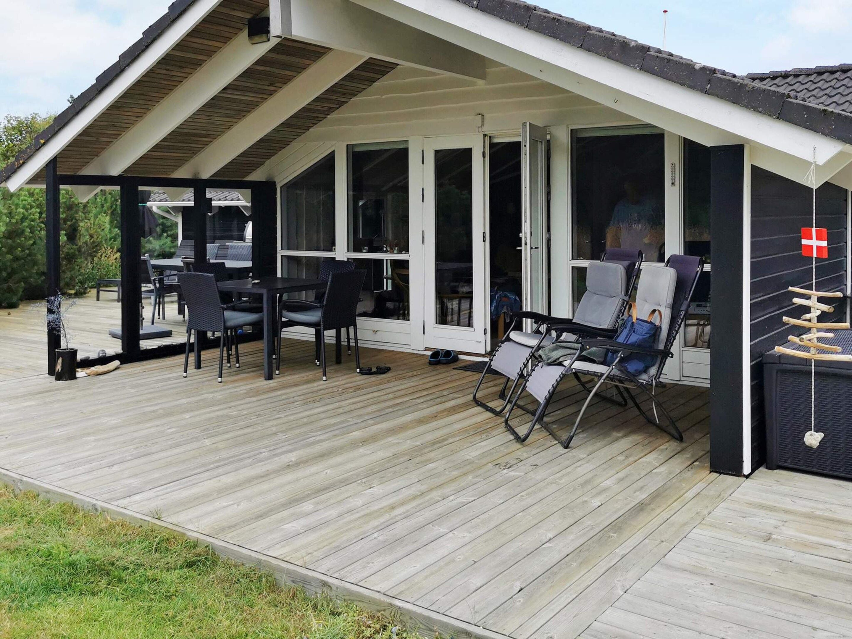 A covered outdoor area with a dining table and chairs, a lounge chair, and a flag.