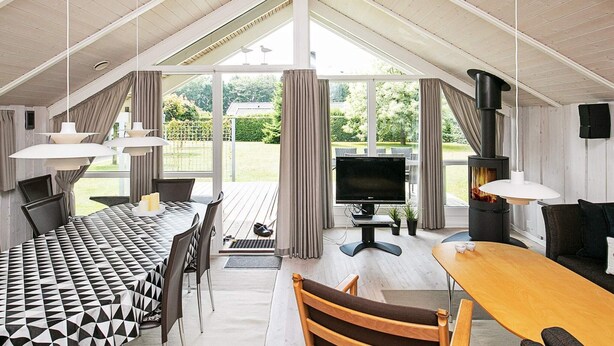A spacious room with a high ceiling, a fireplace, a television, and a dining area with a patterned tablecloth. - 8 Person Holiday Home in Otterup (Otterup)