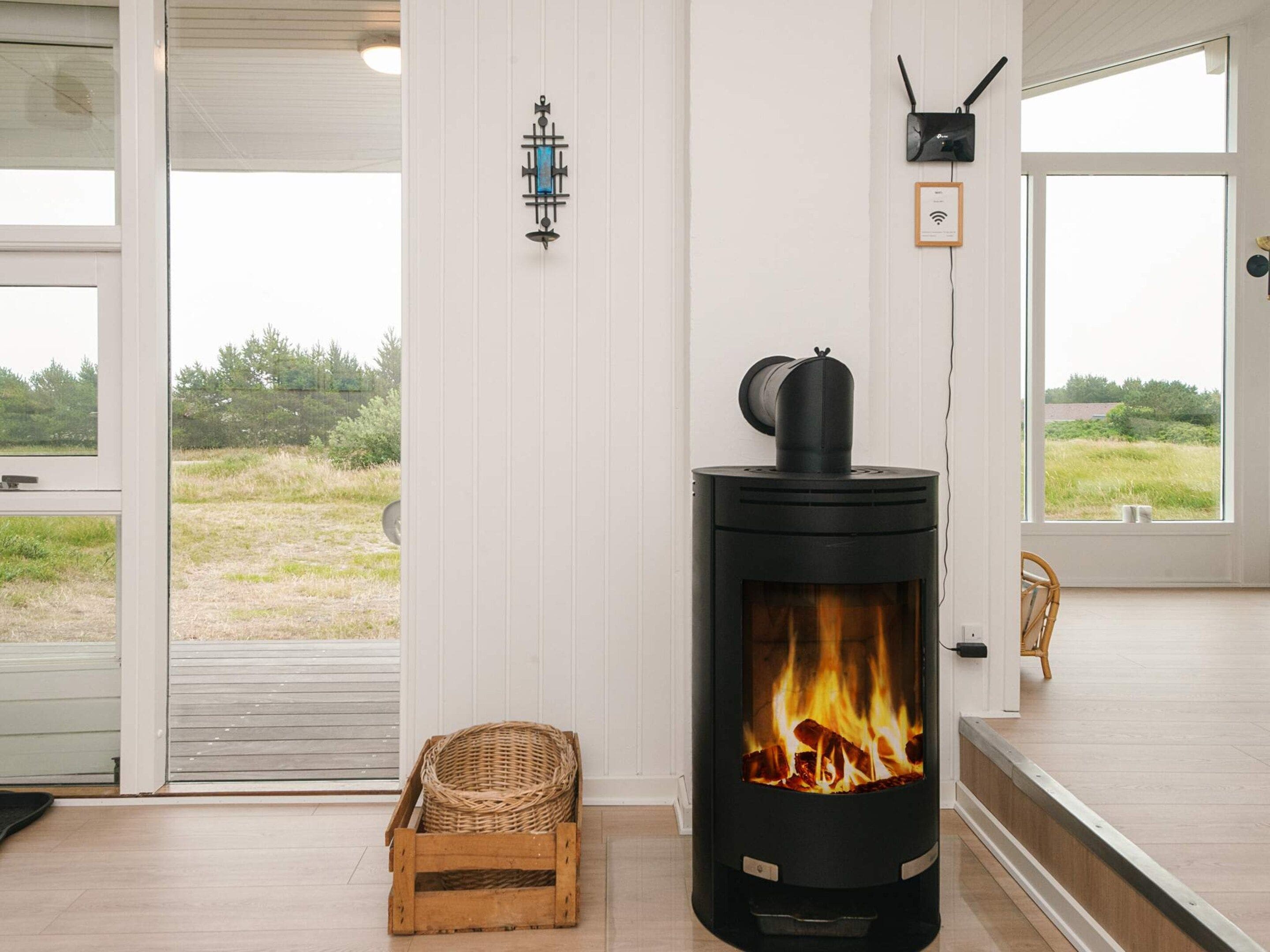 A room with a wood-burning stove, a wicker basket, and a view through a glass door.