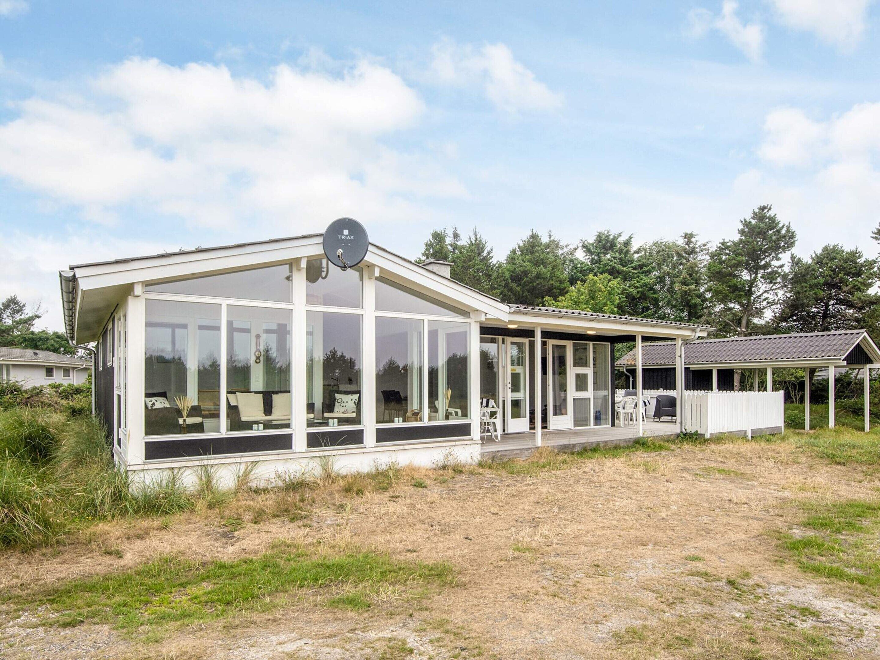 A modern house with large glass windows, a satellite dish, and a covered patio area.