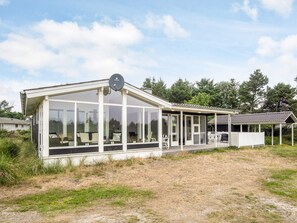 Uma casa moderna com grandes janelas de vidro, uma antena parabólica e uma área de varanda coberta.