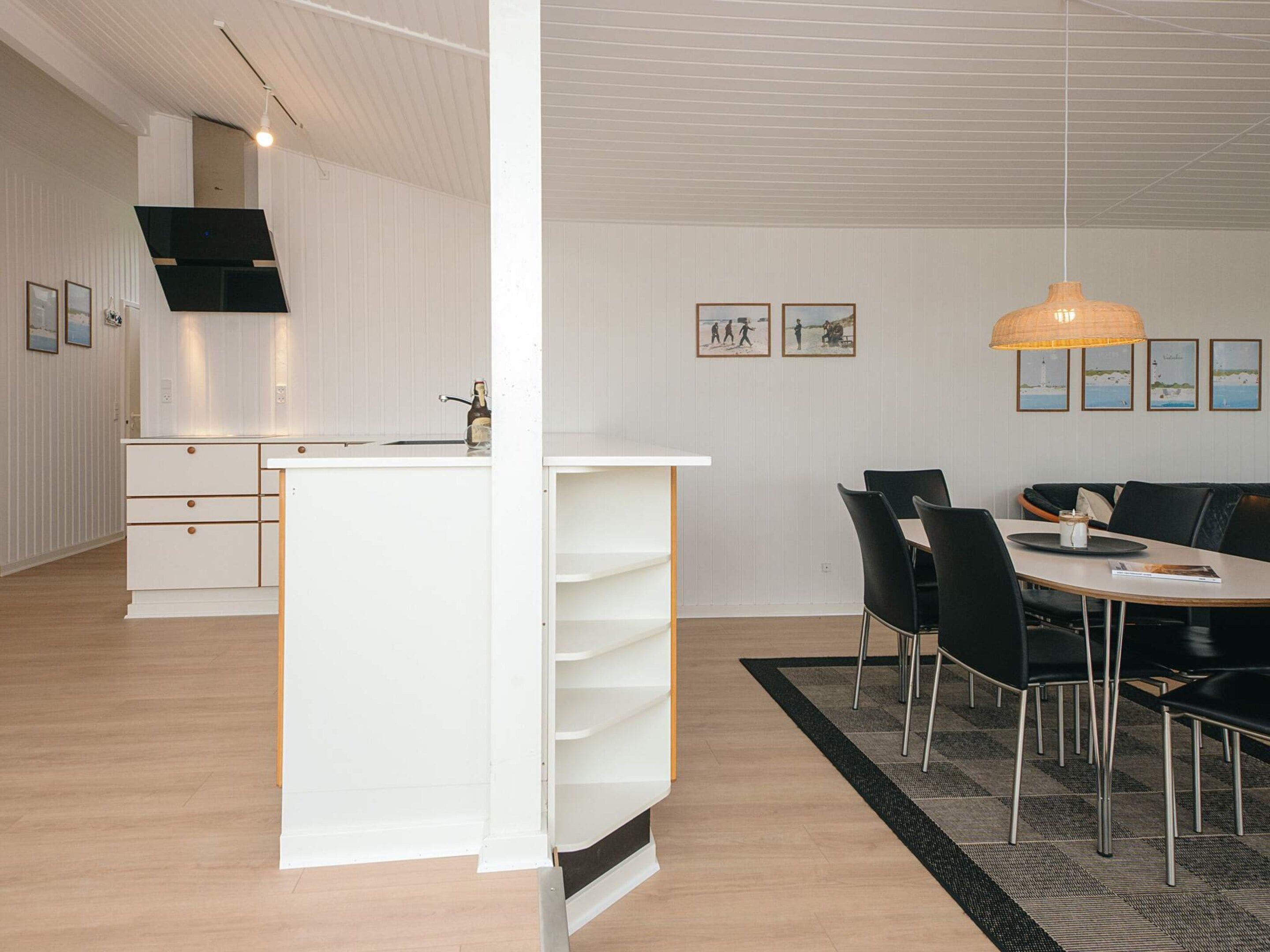 A modern kitchen with white cabinetry and a central island, a dining area with a black table and chairs, and a ceiling with a hanging light fixture.