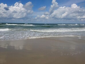 Una playa con olas, arena y un cielo parcialmente nublado.