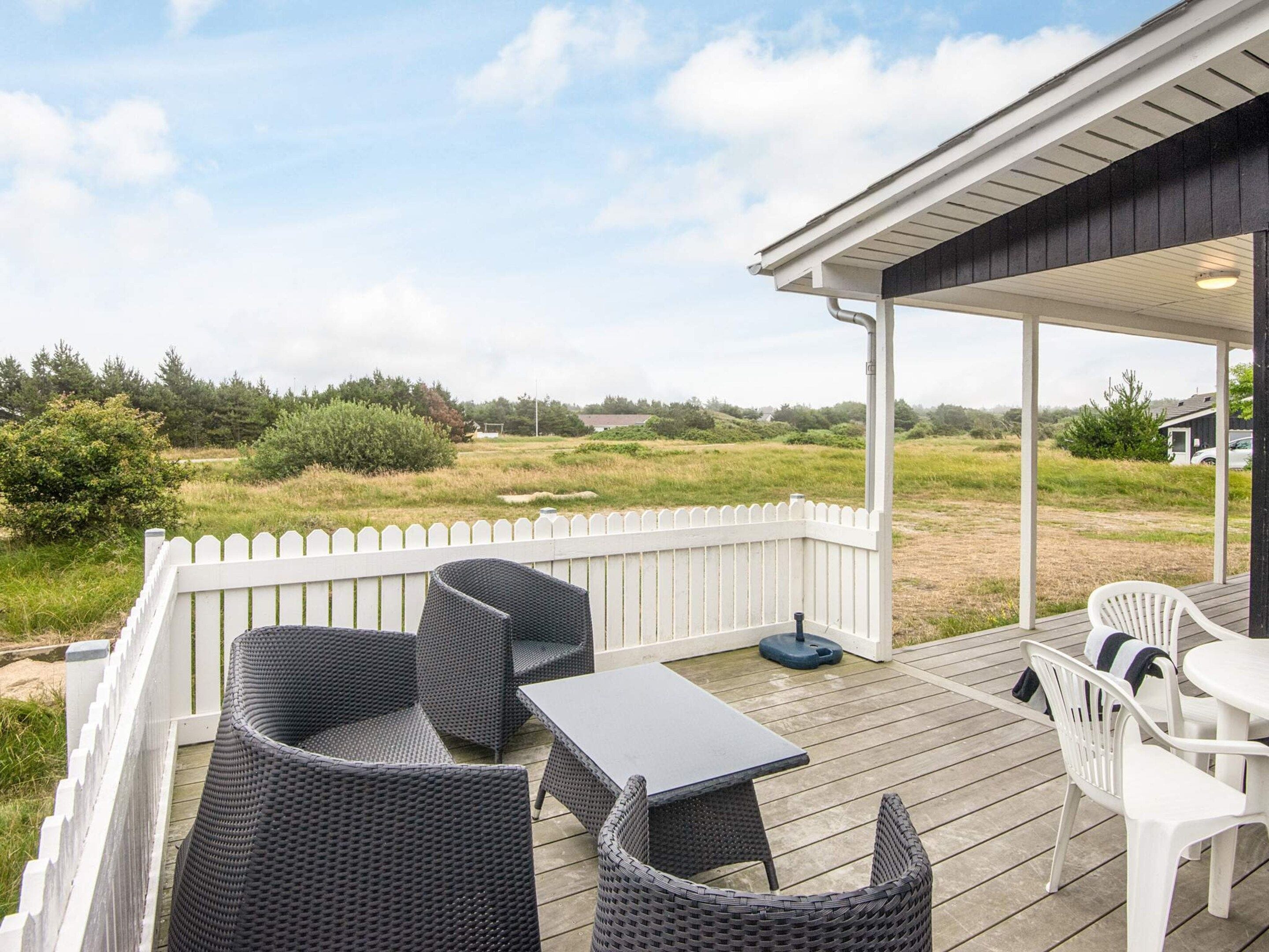 A covered outdoor deck with wicker furniture and a table, overlooking a grassy landscape.