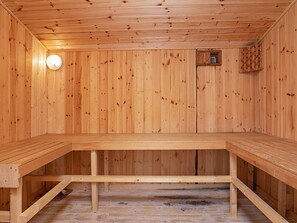 A sauna with wooden walls and benches, a light fixture, and a small window.