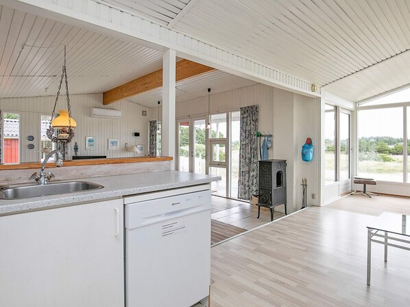 A spacious kitchen with a large island, a hanging pendant light, and a view through the open door.