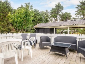Une terrasse extérieure avec des meubles en osier et une clôture blanche en bois.