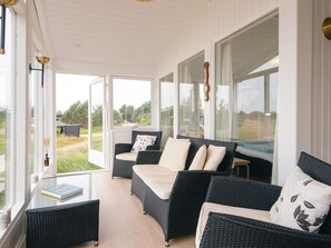 Una habitación iluminada por el sol con muebles de mimbre, ventanas grandes y vistas al exterior.