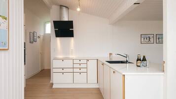 A modern kitchen with white cabinetry, a black range hood, and a wooden floor.