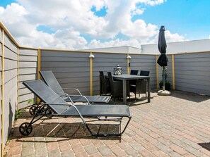 A patio with a table and chairs, a pair of lounge chairs, and a potted plant.