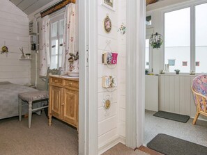 A room with a bed, a wooden dresser, a chair, a wall-mounted shelf with decorative items, and a window with a view of buildings.