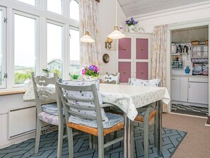 A dining area with a table set for four, chairs with floral upholstery, a pendant light, and a view of the outside.