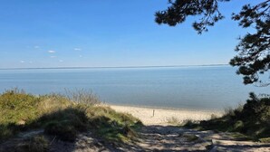 A sandy beach with a wooden pathway leading to the water, surrounded by grass and trees.
