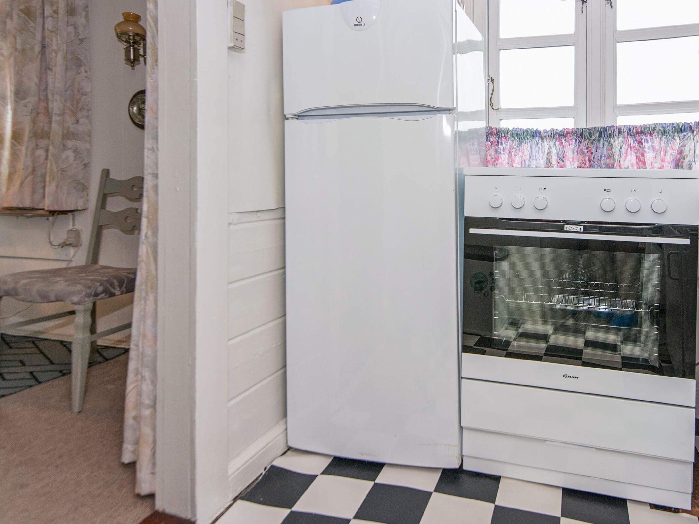 Une cuisine avec un réfrigérateur blanc, un four, un carrelage à motifs et une fenêtre avec un rideau.
