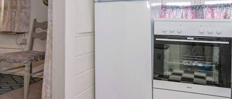 Une cuisine avec un réfrigérateur blanc, un four, un carrelage à motifs et une fenêtre avec un rideau.