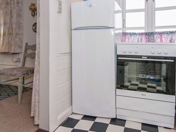 A kitchen with a white refrigerator, an oven, a checkered floor, and a window with a curtain.