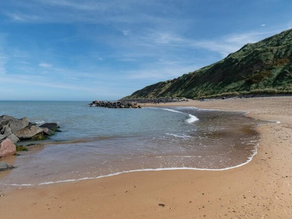 A beach with a rocky breakwater, calm sea, and a sandy shore.