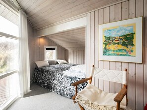 A bedroom with a bed, a window, a chair, and a painting on the wall.