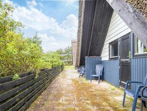 A covered outdoor seating area with a wooden fence, a stone pathway, and chairs. - 6 Person Holiday Home in Blavand (Blavand)