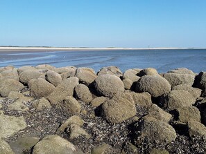 Een rotsachtige kustlijn met grote rotsblokken en kiezels, die uitloopt in een rustige zee.