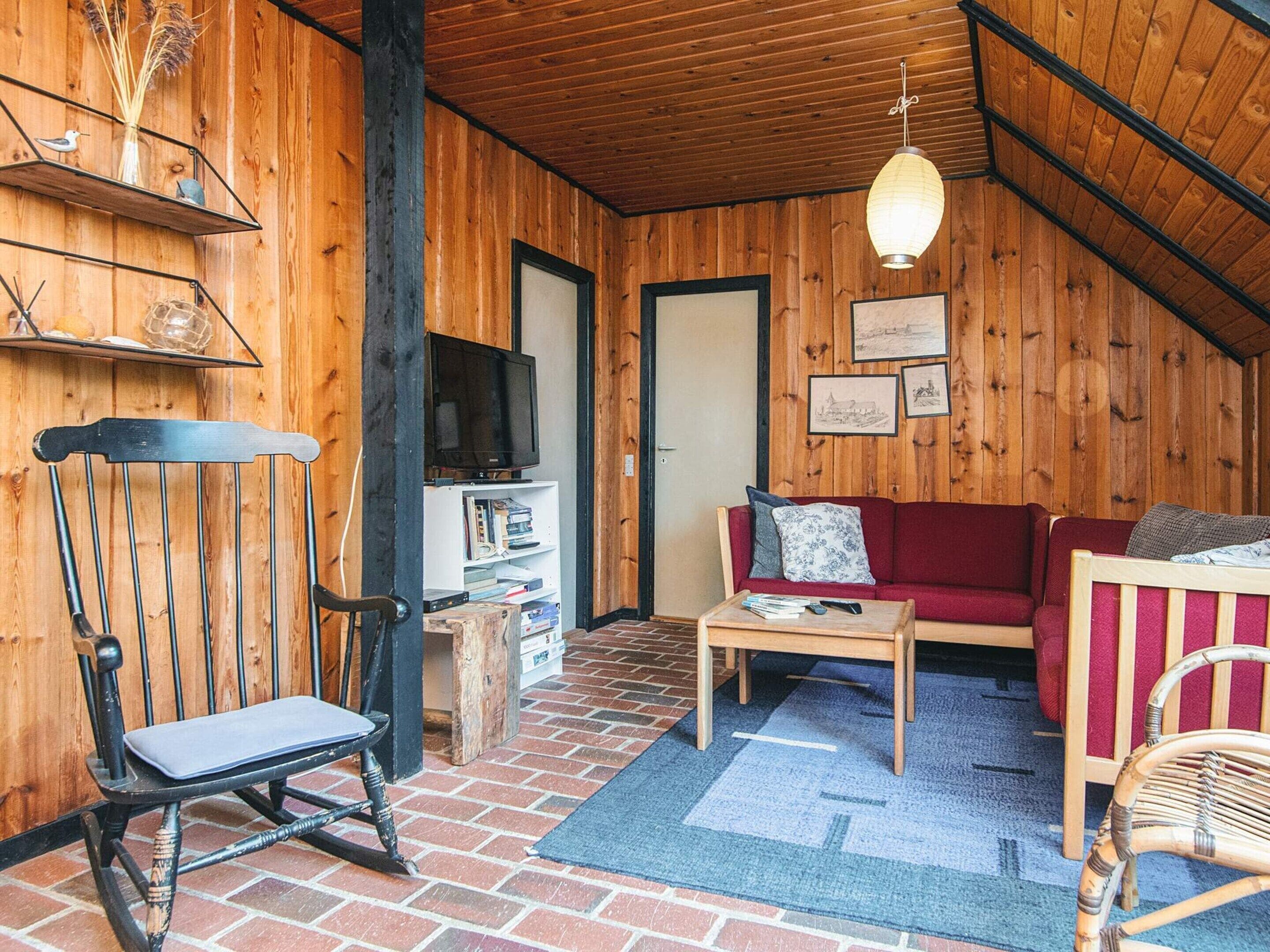 Un interior cálido de madera con un sofá rojo, una silla de madera, una mesita y un televisor en un estante.