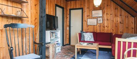 A cozy wooden interior with a red sofa, a wooden chair, a small table, and a television on a shelf.