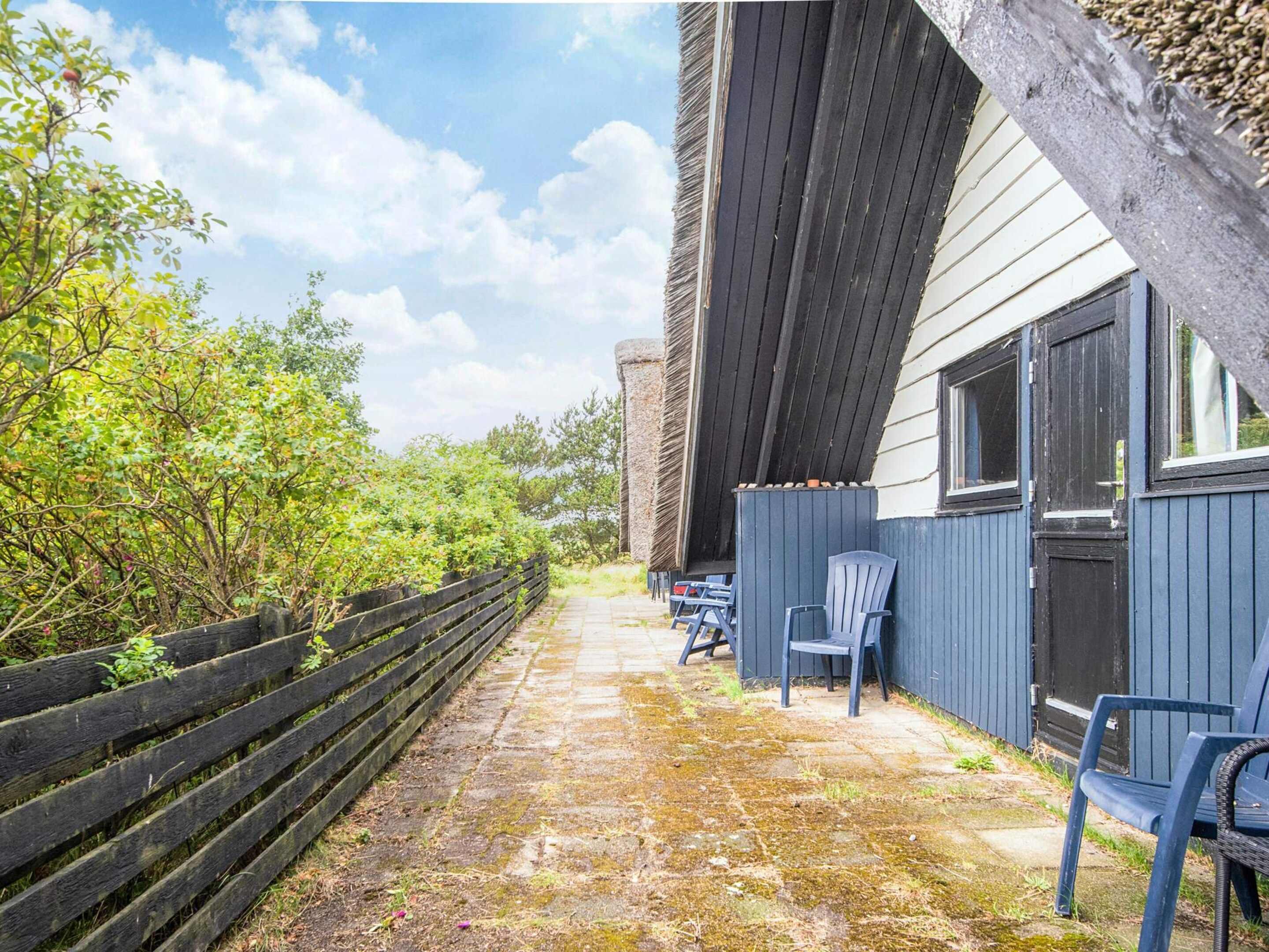 Een terras buiten, met een houten omheining, een pad van stenen en buitenmeubels.