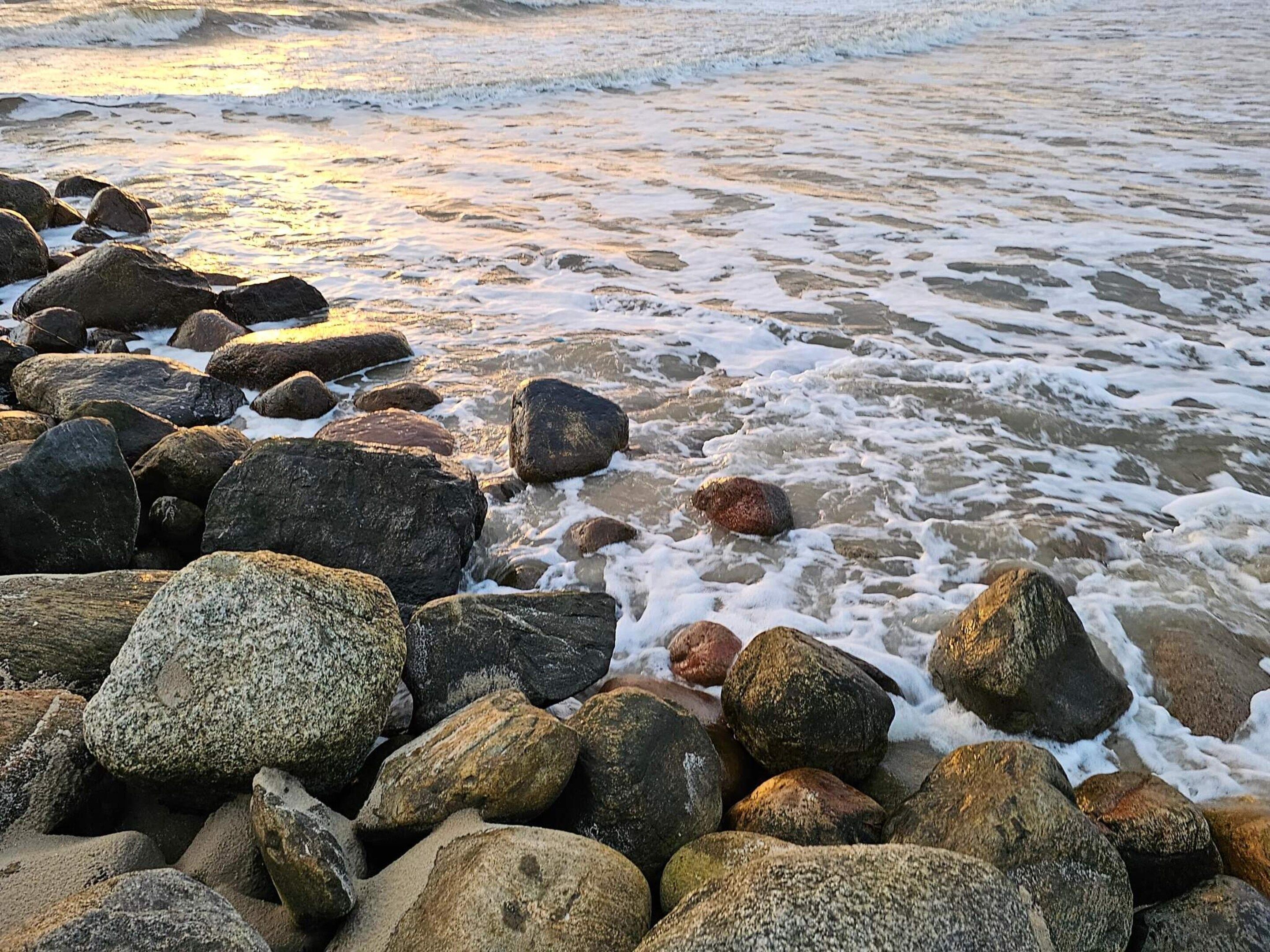 A rocky shoreline with waves gently lapping against the rocks.