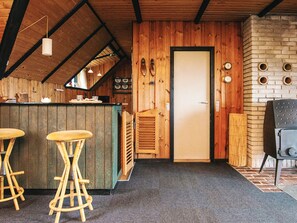 A rustic interior with a wooden bar area, stools, a door, and a brick wall with circular cutouts. - 6 Person Holiday Home in Blavand (Blavand)