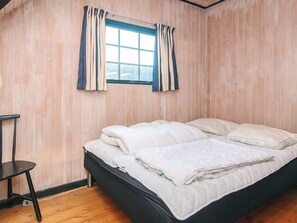Een slaapkamer met een houten wand, een raam met gordijnen, een bed met witte beddengoed en een kleine tafel.
