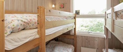 A bunk bed room with wooden walls, a window with a view, and a radiator.