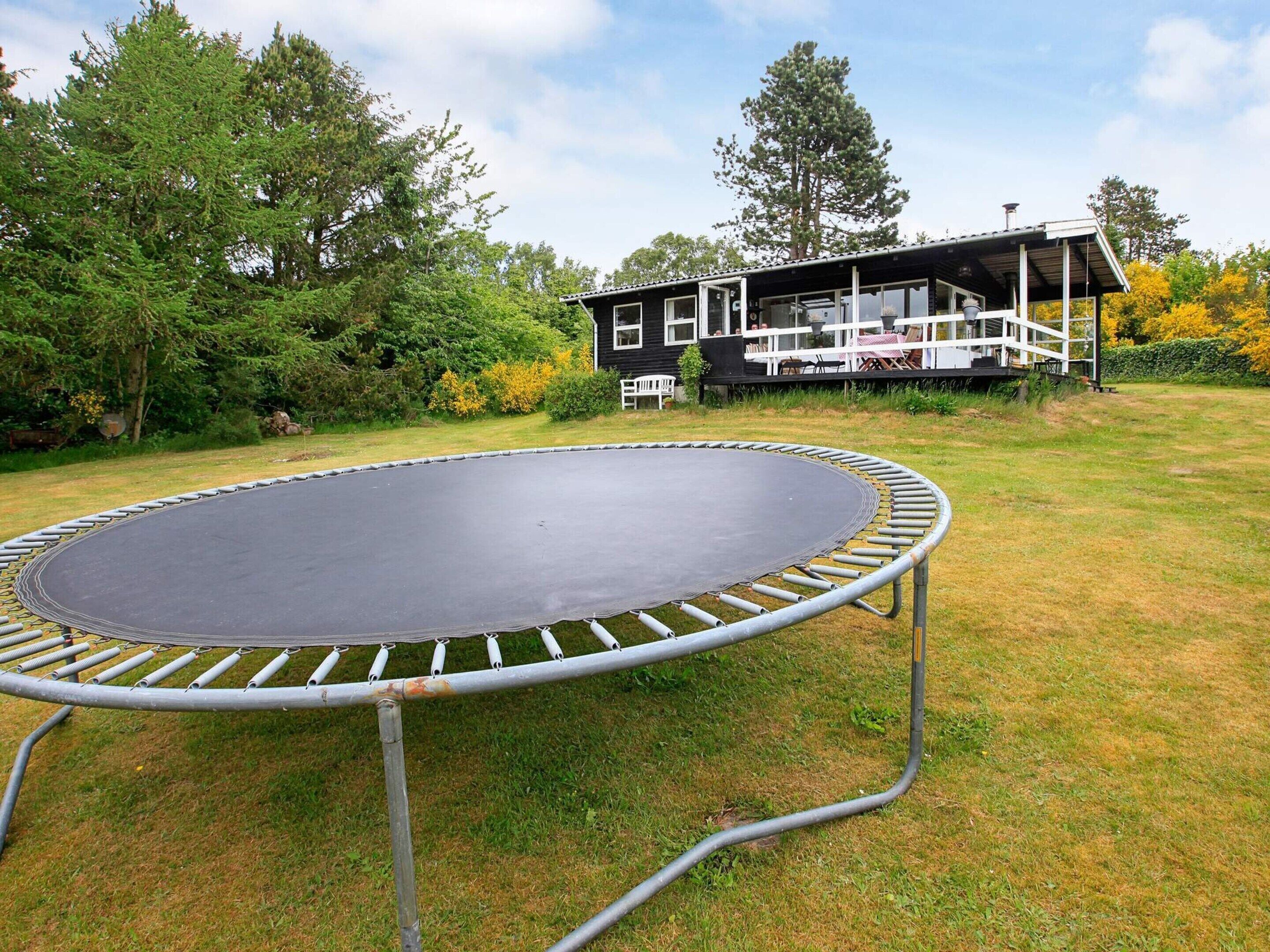 A trampoline in a grassy yard with a house in the background.