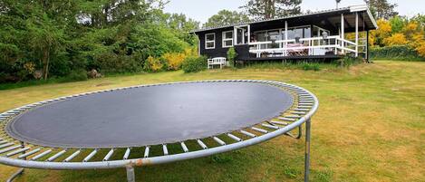 A trampoline in a grassy yard with a house in the background.