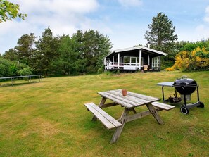 Un montaje para picnic con una mesa y bancos de madera, una parrilla y una casa al fondo.