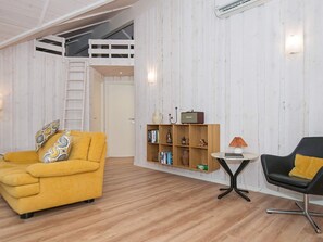A room with a yellow sofa, a black chair, a small table, and a bookshelf. - Splendid Holiday Home in Jutland With Whirlpool (Sydals)