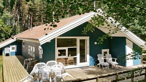 En hytte med terrasse, hvide plastikstole og et stort vindue.