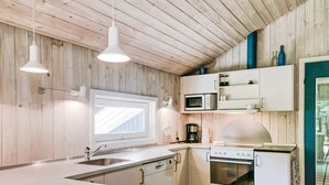 Cozinha moderna com painéis de madeira, uma ilha grande, armários brancos, micro-ondas, fogão e iluminação pendente.