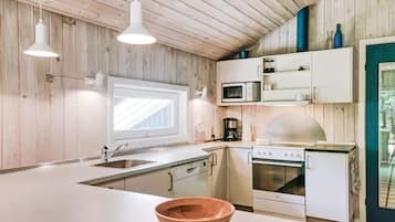 Et moderne køkken med træpaneler, en stor ø, hvide skabe, en mikroovn, en komfur og hængende lamper.