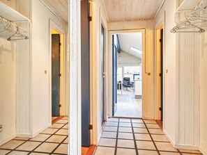 Un pasillo con paredes blancas y suelo de baldosas que conduce a una habitación con un escritorio y una silla.