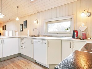 A modern kitchen with wooden paneling, a built-in dishwasher, and a window with a view. - 5 Star Holiday Home in Nexo (Akirkeby)