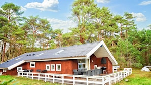 En træhytte med veranda, udendørs møbler og grillområde.