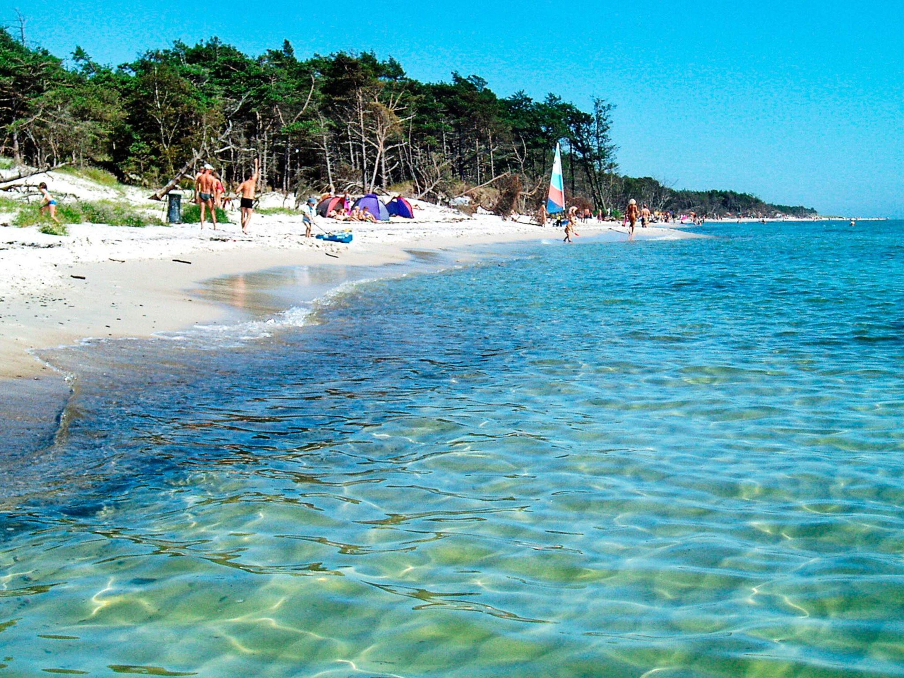 A beach with clear water, tents, and people.
